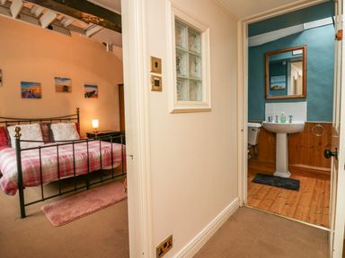 A hallway leading to a bedroom with a metal bed frame and a bathroom with a pedestal sink at Gardeners Cottage in Millom Cumbria