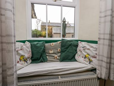 A window seat with cushions and pillows beside a window with plaid curtains at Gardeners Cottage in Millom Cumbria