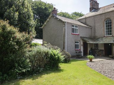 An exterior view of a house with a garden featuring bushes a gravel area and outdoor seating at Gardeners Cottage Millom Cumbria