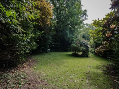 A grassy garden area with shrubs and trees surrounding the space at Gardeners Cottage in Millom Cumbria