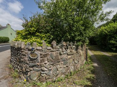 A stone wall with plants behind it and a sign saying Millholme House next to a narrow path at Gardeners Cottage in Millom Cumbria