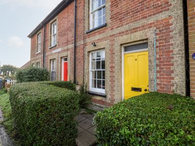 A row of brick cottages with a yellow door and a red door and trimmed hedges outside 3 Albion Cottages Walberswick