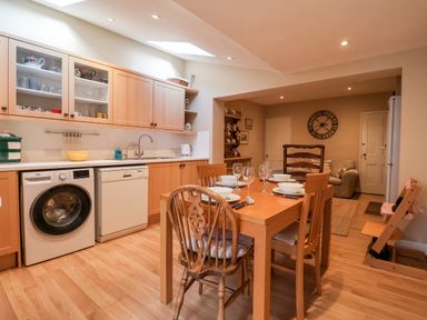 A kitchen and dining area with wooden cabinets a dining table with chairs and a sofa in the background at 3 Albion Cottages in Walberswick
