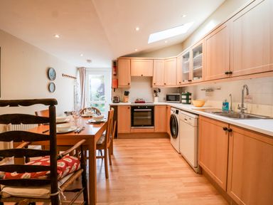 A kitchen with wooden cabinets a dining table set with bowls and cutlery and appliances at 3 Albion Cottages in Walberswick