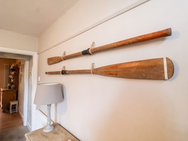 Two wooden oars mounted horizontally on a wall above a table with a lamp in a hallway at 3 Albion Cottages in Walberswick