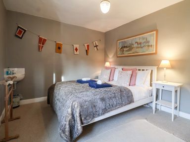 A bedroom with a double bed two bedside tables with lamps and nautical flags on the wall at 3 Albion Cottages in Walberswick