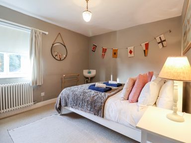 A bedroom with a bed with pillows and towels bedside table with lamp a window with curtains and a radiator at 3 Albion Cottages in Walberswick