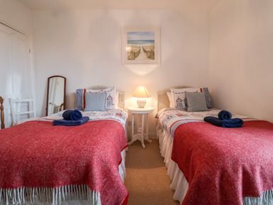 A bedroom with two single beds with red blankets and blue towels a bedside table with a lamp a wall mirror and a picture above the beds at 3 Albion Cottages Walberswick