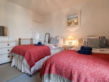 A bedroom with two single beds covered with red blankets and blue towels at 3 Albion Cottages in Walberswick
