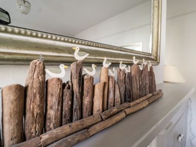 Wooden duck decorations on driftwood on a cabinet below a mirror at 3 Albion Cottages in Walberswick