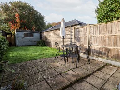 A backyard with a patio table and chairs and a closed umbrella near a wooden fence and a garden shed at 3 Albion Cottages in Walberswick