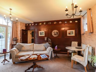 A sitting room with a sofa, two side tables, a coffee table, two chairs at a round table, and a dark wood paneled wall at The Barn in Middleton near Ponteland