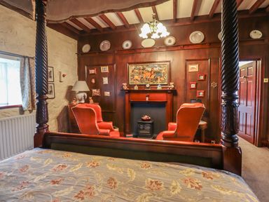 A bedroom with a four-poster bed two armchairs a fireplace and wood-paneled walls at The Barn in Middleton near Ponteland