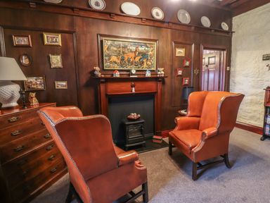 A sitting room with two orange leather armchairs a fireplace wooden paneling and framed pictures at The Barn in Middleton near Ponteland