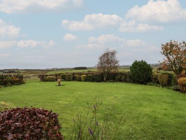 A garden with a lawn, bushes, small trees, and a view of fields at The Barn in Middleton near Ponteland