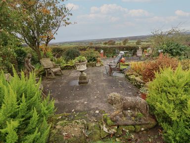 An outdoor garden patio with chairs planters a lion statue and a human skeleton figure seated at The Barn in Middleton near Ponteland