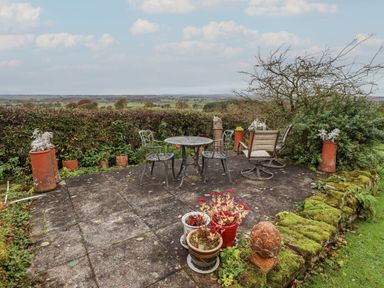 An outdoor patio area with metal table and chairs surrounded by potted plants and greenery at The Barn in Middleton near Ponteland