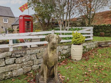 A garden area with a stone dog statue a white wooden fence a red telephone box and a barrel planter at The Barn in Middleton near Ponteland