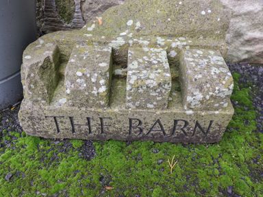 A stone block with the inscription THE BARN standing on mossy ground in Middleton near Ponteland