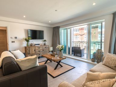 A living room with sofas a wooden coffee table and a TV on a wooden cabinet by sliding glass doors at 31 Cliff Edge in Newquay