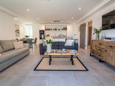 A modern open plan living room with two sofas a wooden coffee table a sideboard a dining area and kitchen at 31 Cliff Edge in Newquay