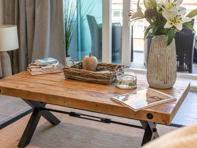 A wooden coffee table with books a vase of flowers a candle and a wicker tray in a living room at 31 Cliff Edge in Newquay