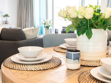 A dining table set with white bowls and plates on woven placemats with a vase of white flowers in a living room at 31 Cliff Edge in Newquay