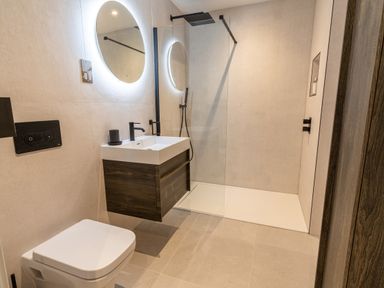 A bathroom with a toilet sink vanity shower area and round illuminated mirror at 31 Cliff Edge in Newquay