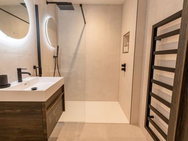 A modern bathroom with a walk-in shower a white sink with a black faucet a round mirror and a black towel rack at 31 Cliff Edge in Newquay