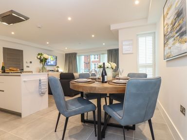 A dining area with a round wooden table and four blue chairs next to an open kitchen and living room at 31 Cliff Edge in Newquay