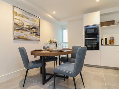 A dining area with a wooden round table set with plates and glasses and four blue chairs at 31 Cliff Edge in Newquay