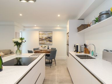 A kitchen with white countertops a sink and an electric stove next to a dining area with a round table and four chairs at 31 Cliff Edge in Newquay