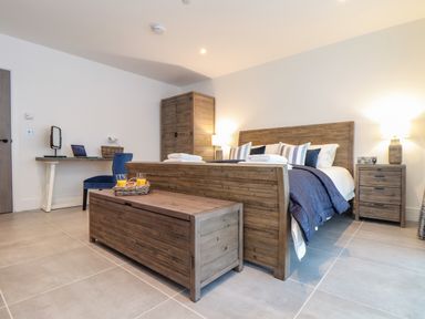 A bedroom with wooden bed frame and chest at the foot of the bed a wooden wardrobe a bedside table with lamp and a desk with chair at 31 Cliff Edge in Newquay