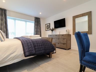 A bedroom with a bed folded towels a wooden dresser a wall-mounted TV and two blue chairs at 31 Cliff Edge in Newquay