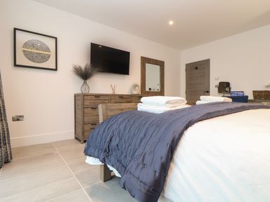 A bedroom with a bed covered by a blue blanket and folded towels on top a wooden dresser with decorative items a wall-mounted TV and a wall mirror at 31 Cliff Edge in Newquay