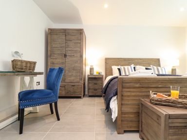 A bedroom with wooden bed frame and wardrobe blue chair and side tables at 31 Cliff Edge in Newquay