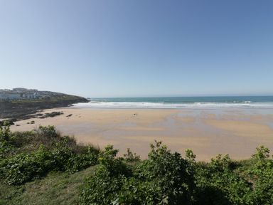 A sandy beach with waves and greenery in the foreground at 31 Cliff Edge in Newquay