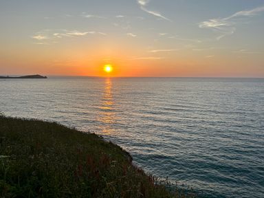 A sunset over the ocean with a grassy cliff in the foreground at 31 Cliff Edge in Newquay