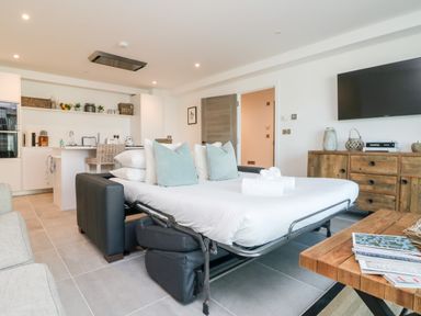 A living area with a sofa bed extended with pillows and towels in front of a wooden cabinet and wall mounted TV at 31 Cliff Edge in Newquay