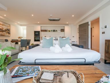 A living space with a sofa bed in the center, dining table, kitchen in the background, and wooden cabinet at 31 Cliff Edge in Newquay