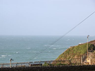 A view of the ocean with a metal fence and a viewing telescope on a stone wall by a grassy hillside at 31 Cliff Edge in Newquay