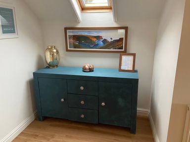 A blue cabinet with decorative items under a skylight and a framed landscape photograph on the wall at Harbour Light in Boscastle