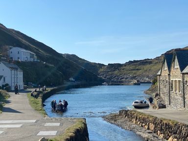 A coastal inlet with a group of people near the water and boats along the shore at Harbour Light in Boscastle