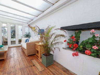 A sunroom with wooden flooring a wicker sofa a wooden side table plants and flowers at Harbour Light in Boscastle
