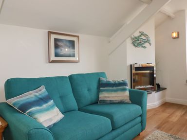 A turquoise sofa with striped cushions a wall-mounted fish decoration and a fireplace in a living room at Harbour Light in Boscastle