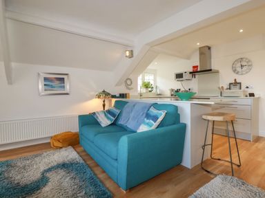 A living room with a blue sofa and pillows next to a kitchen with a stool at Harbour Light in Boscastle