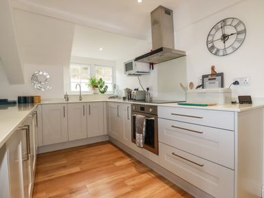 A kitchen with cabinets a stove microwave bread box and wall clock at Harbour Light in Boscastle