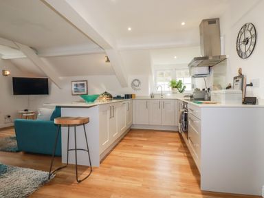 A kitchen with white cabinets and wooden floor connected to a living area with a teal sofa at Harbour Light in Boscastle