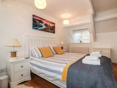 A bedroom with a double bed striped bedding bedside tables lamps and a window at Harbour Light Boscastle