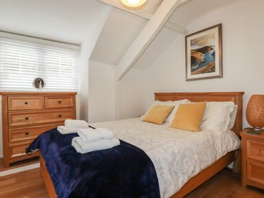 A bedroom with a bed with folded towels a wooden dresser and a nightstand with a lamp at Harbour Light in Boscastle